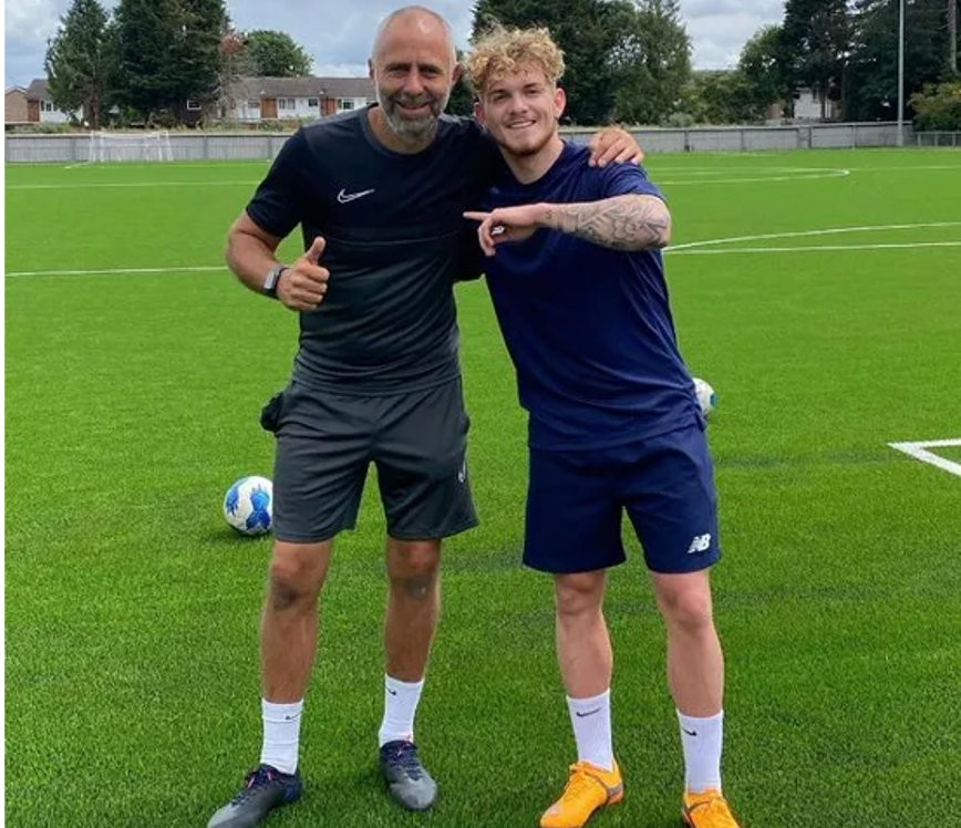 A football coach standing next to a male footballer.