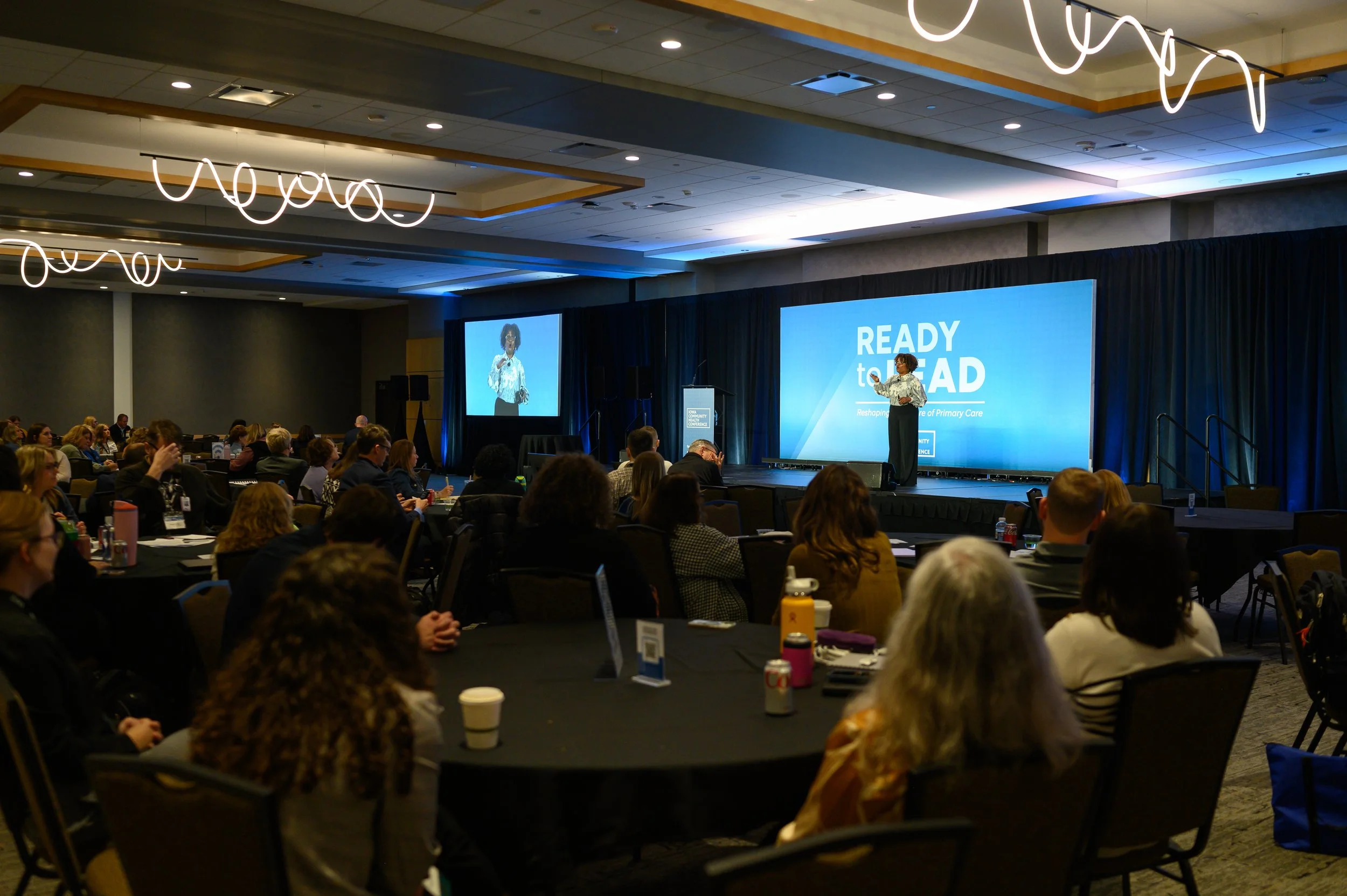 Woman stands on stage in front of ballroom of people sitting at tables