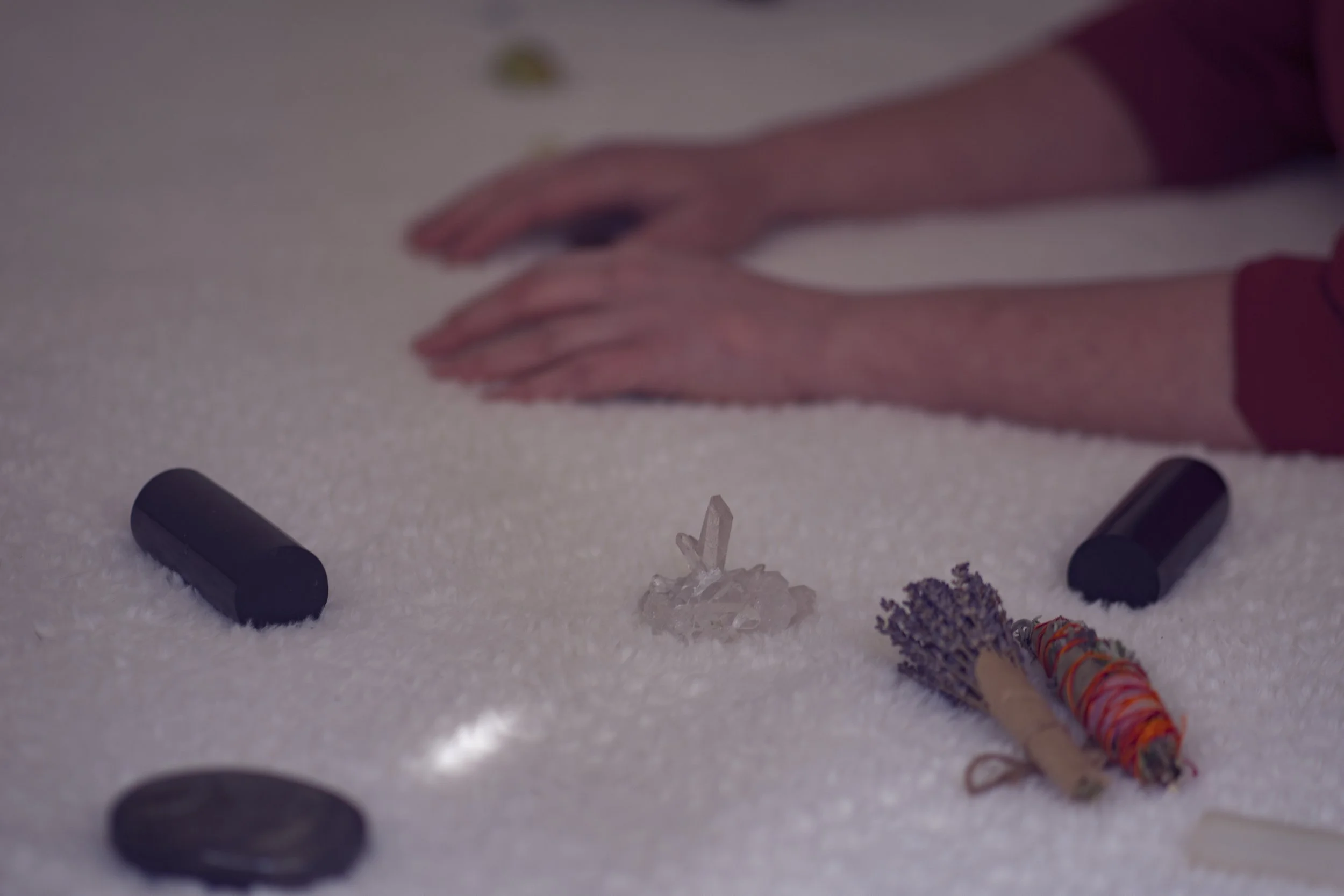 Hands reaching out over a surface with various small objects including candles, wrapped bundles, and a decorative crystal.