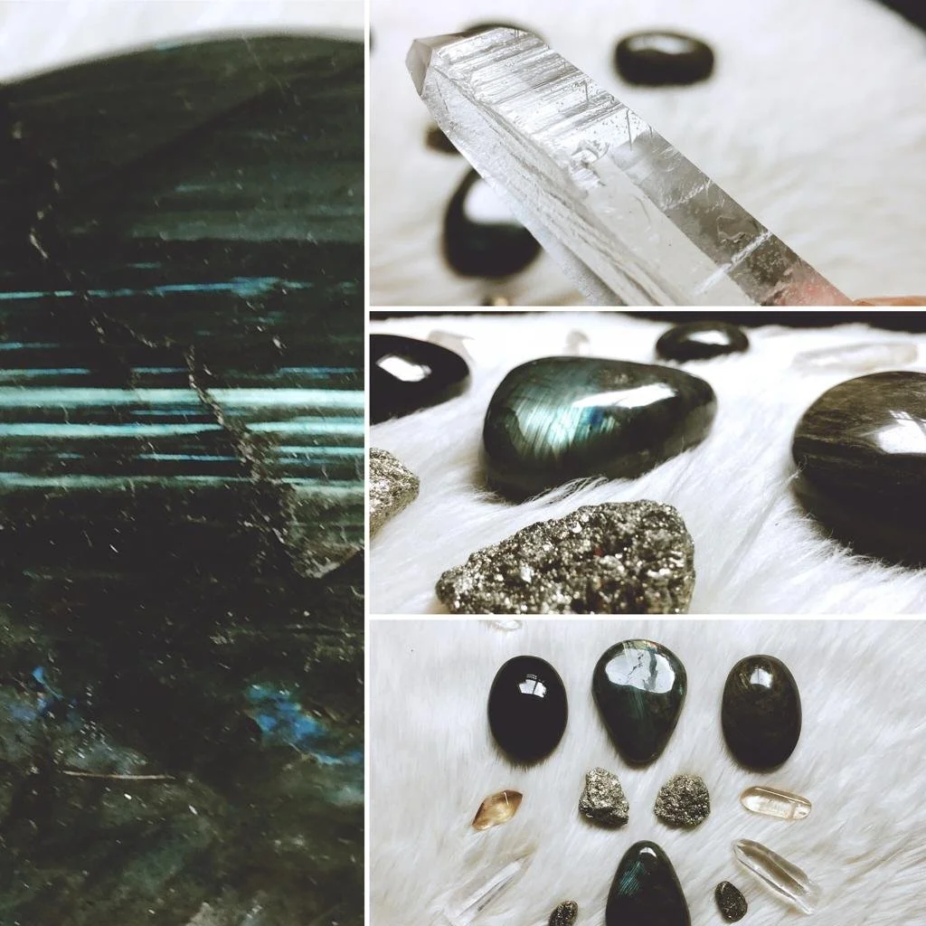 A collection of various gemstones and minerals, including polished black stones, a metallic mineral, and a clear crystal, arranged on a white furry surface.