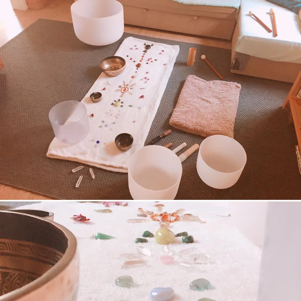 Arrangement of crystal singing bowls, a cloth with embroidery, candles, and soft pillows on a carpeted floor for meditation or sound healing.
