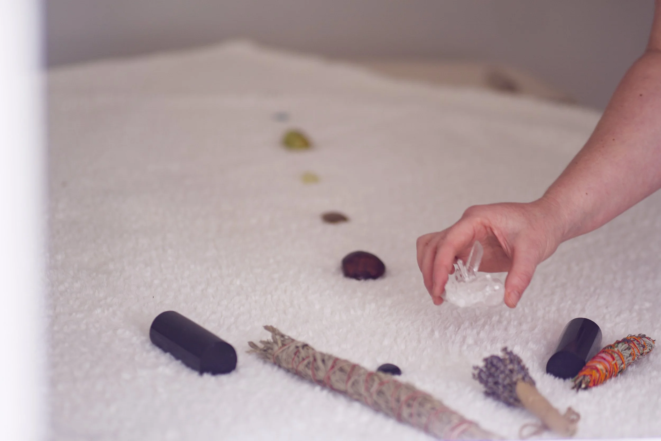 A person arranging objects on a white textured surface, including cylindrical stones, a small crystal, and decorated sticks.