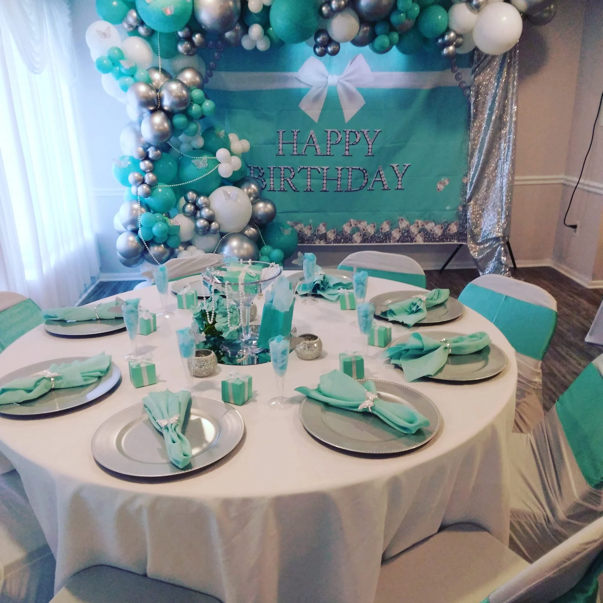 Teal, silver, and white birthday table setup at A Level Up Rental Hall with coordinated linens, balloons, place settings, and backdrop.