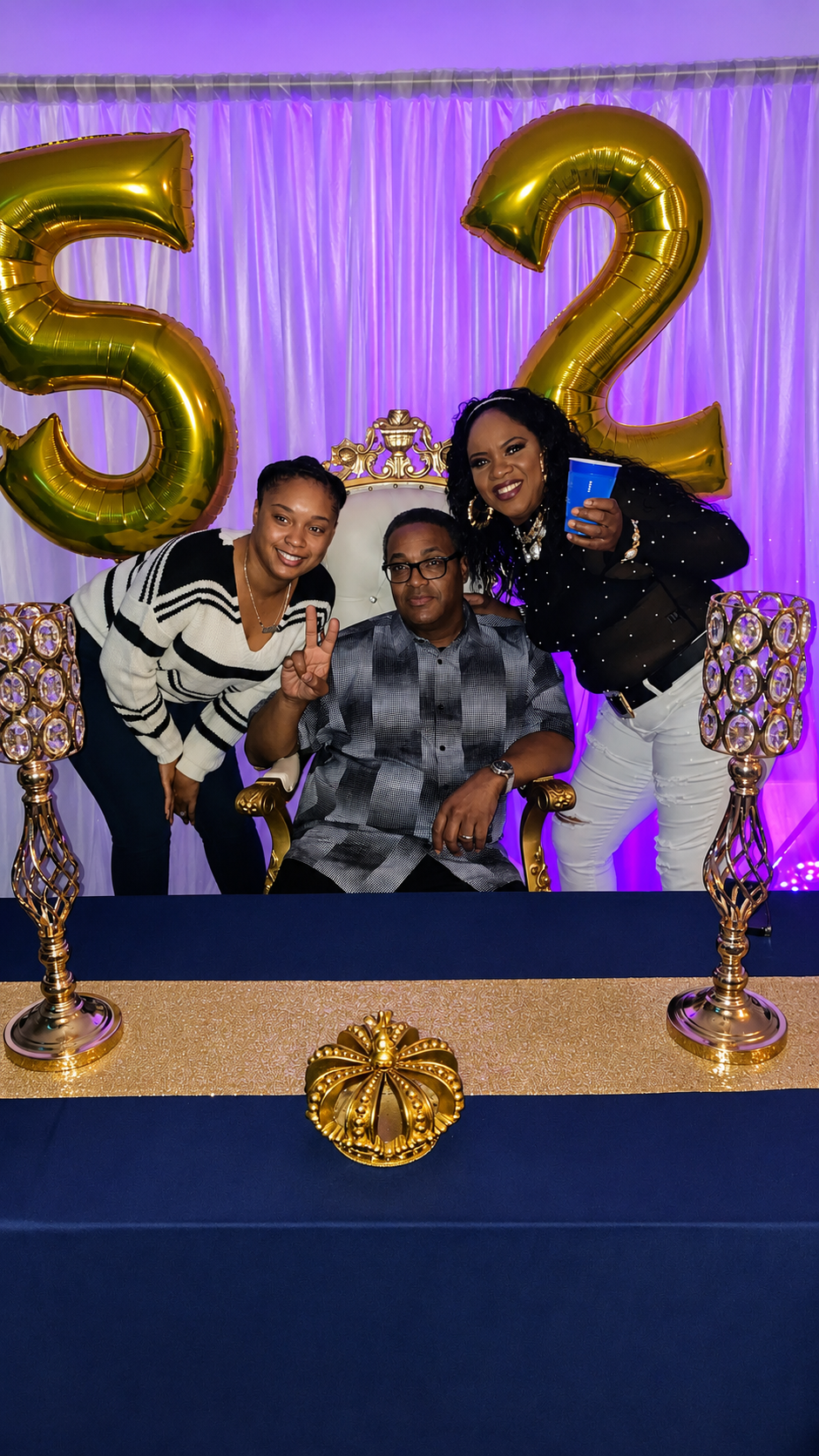 Guests celebrating a 52nd birthday at A Level Up Rental Hall with gold number balloons, purple lighting, and an ornate throne chair.