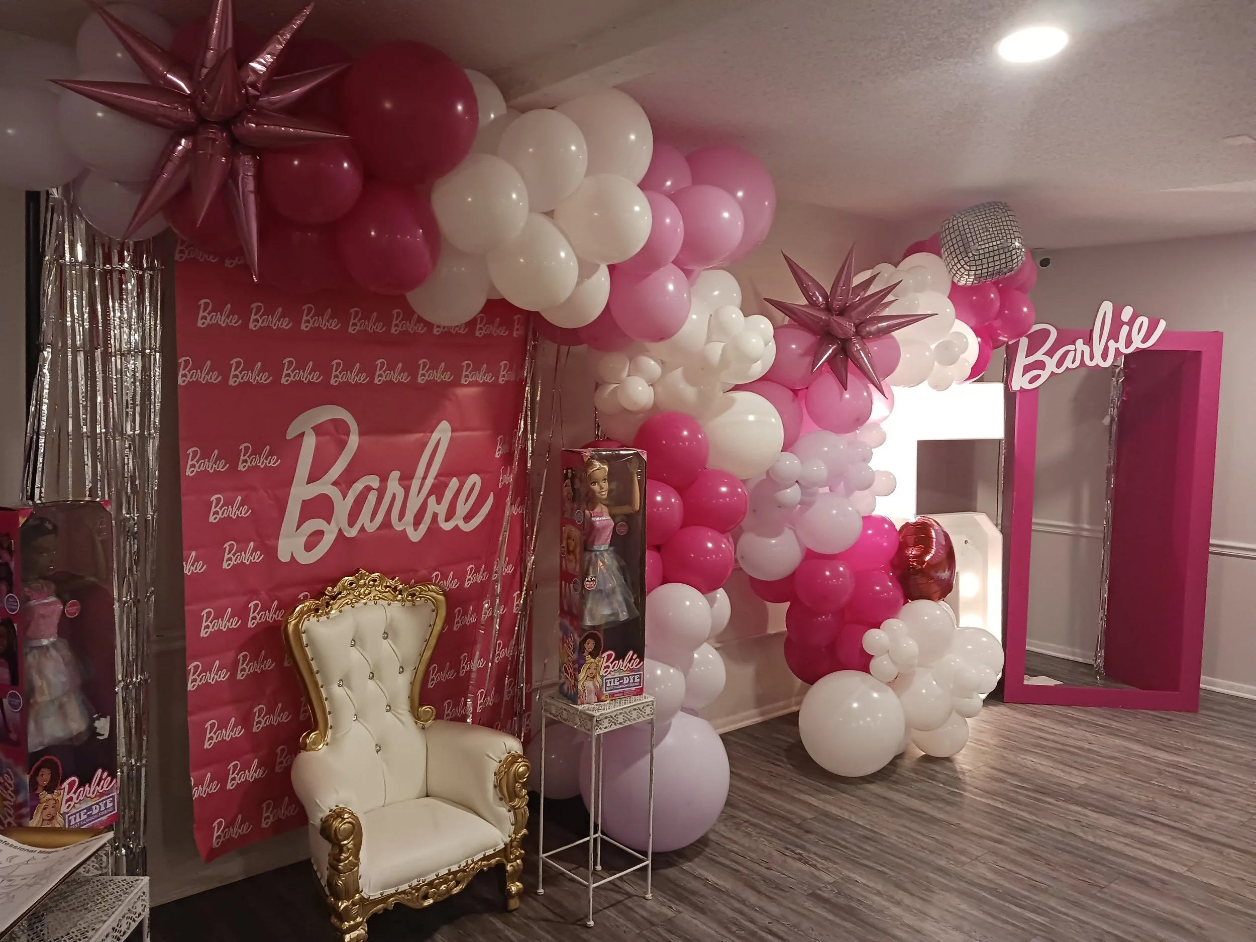 Pink Barbie-themed birthday setup at A Level Up Rental Hall with a balloon garland, white throne chair, and custom backdrop.