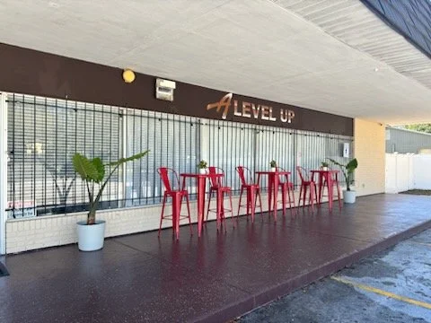 Front entrance of A Level Up Rental Hall in Tampa with covered outdoor seating, red chairs, cocktail tables, and potted plants.