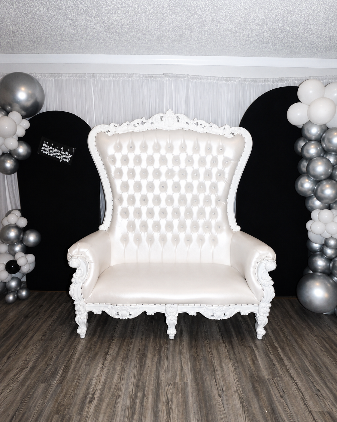 White throne chair with black backdrop panels and silver and white balloon decor at A Level Up Rental Hall.