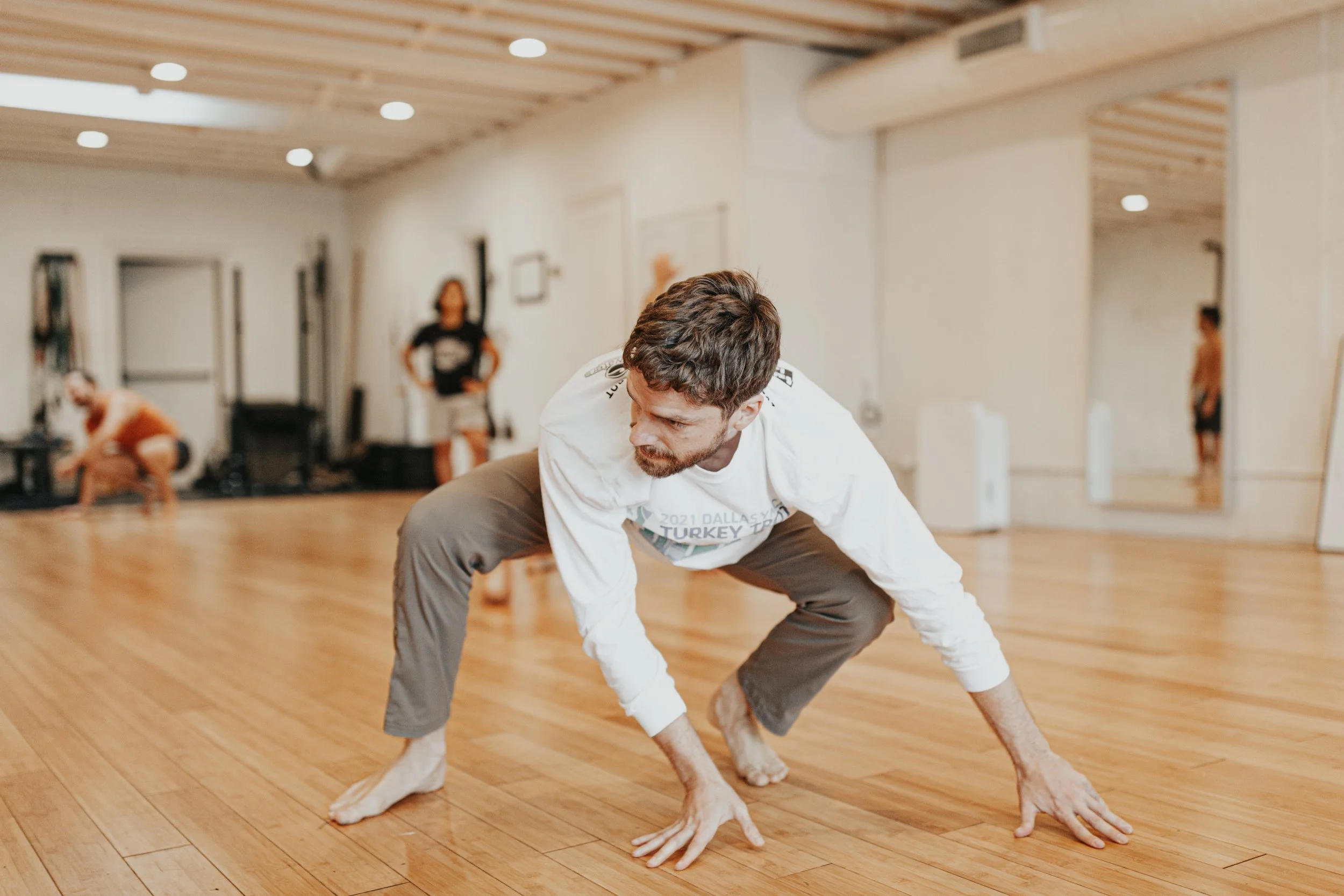 A man and a dog practicing yoga together in a studio, with the man in a yoga pose and the dog on the floor, both focused on their activity.