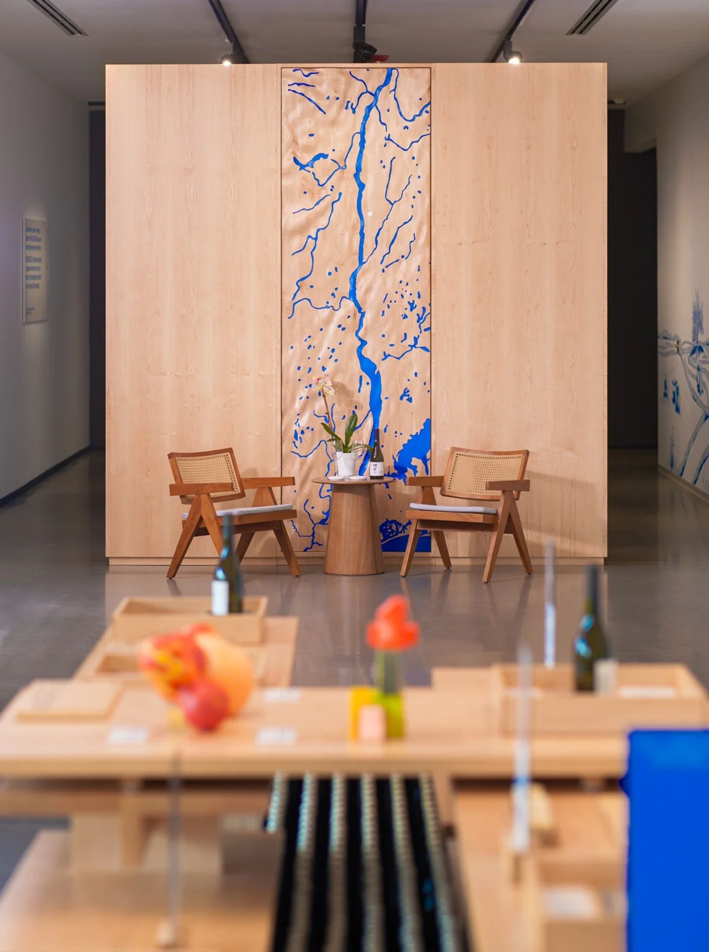 wooden-chairs-and-table-with-blue-river-design-backdrop-in-a-modern-exhibition-space.jpg.webp