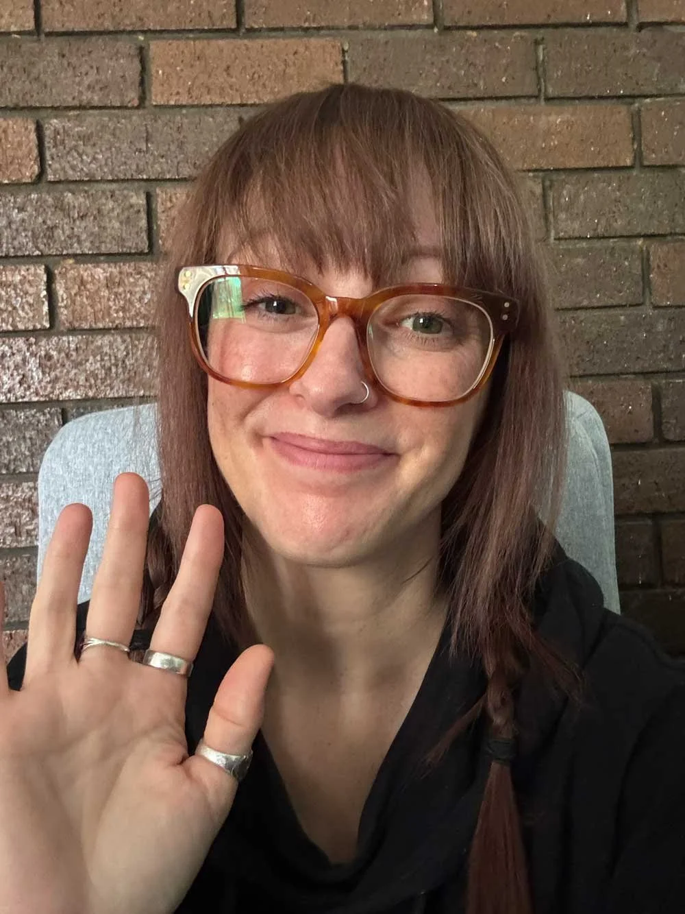 Head and shoulders image of a woman smiling. Her hand is up waving