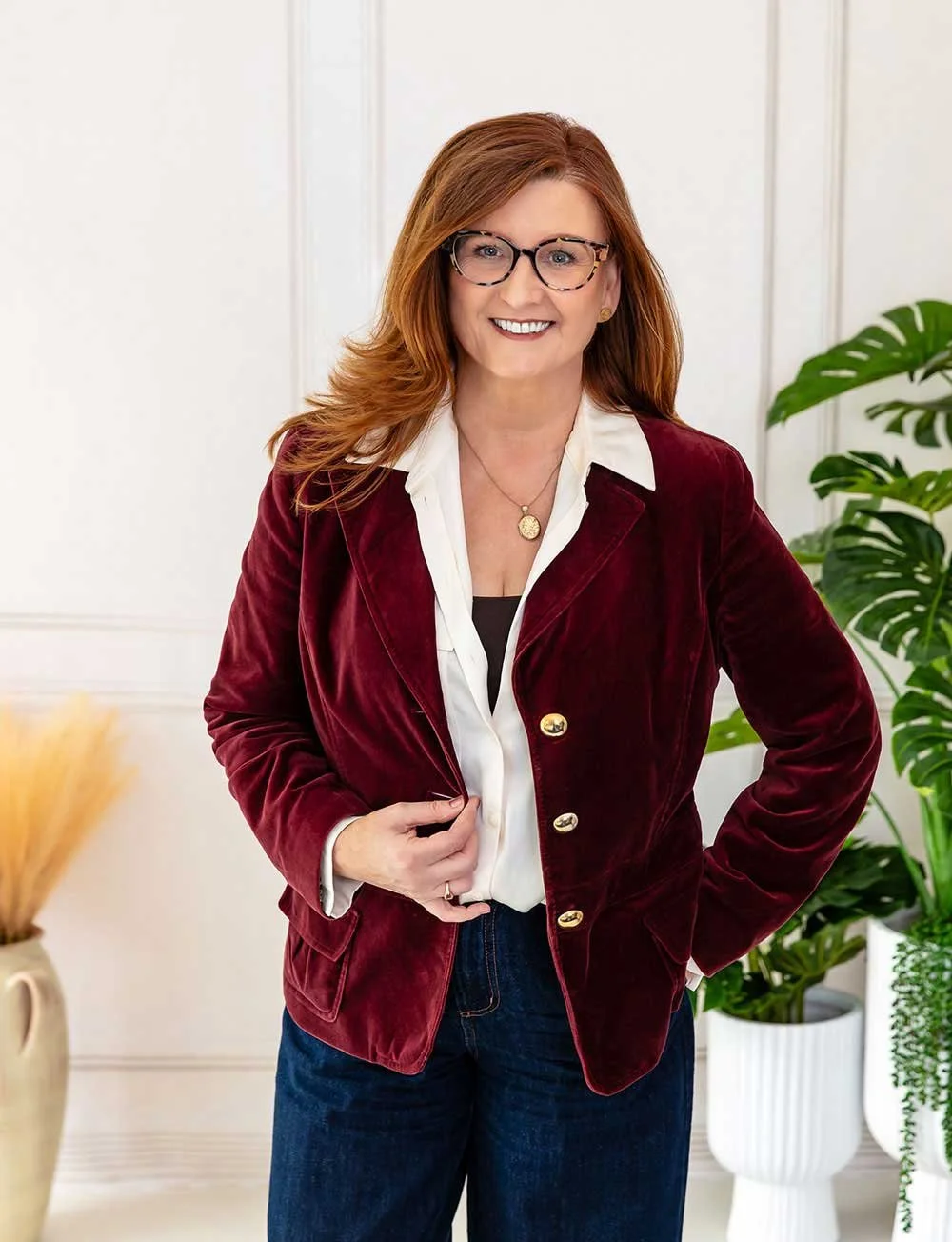 A woman stands smiling with her hand on her maroon blazer