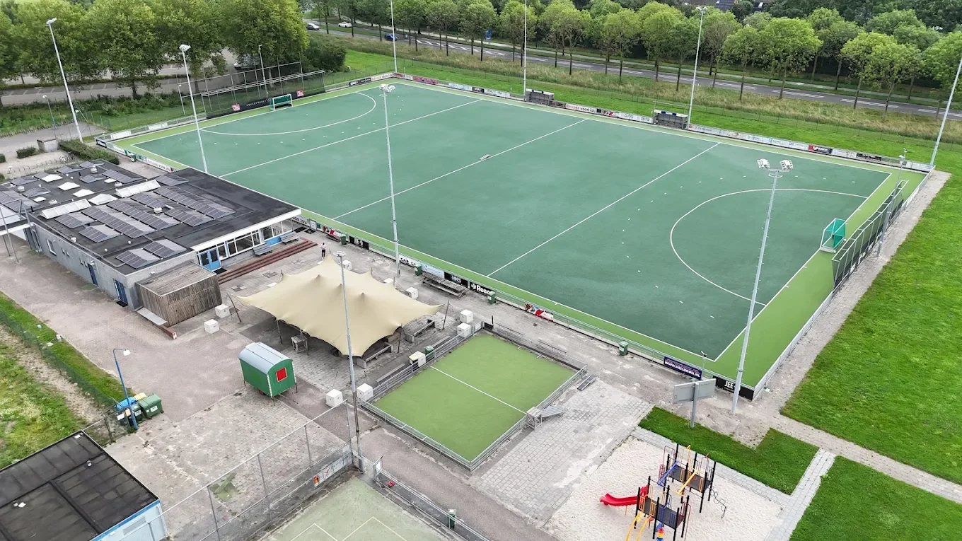 Aerial view of an outdoor hockey field with a smaller hockey practice area in front, surrounded by trees and a road.