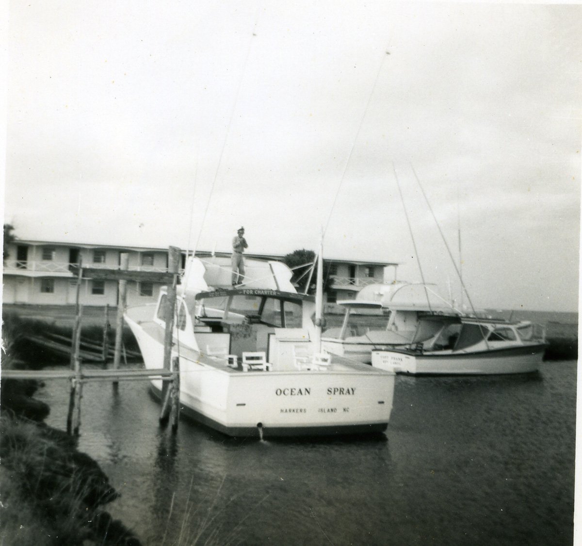 Capt Benny Rose aboard his charter boat, the Ocean Spray, in front of the Carl Lewis Motel, late 1950s.