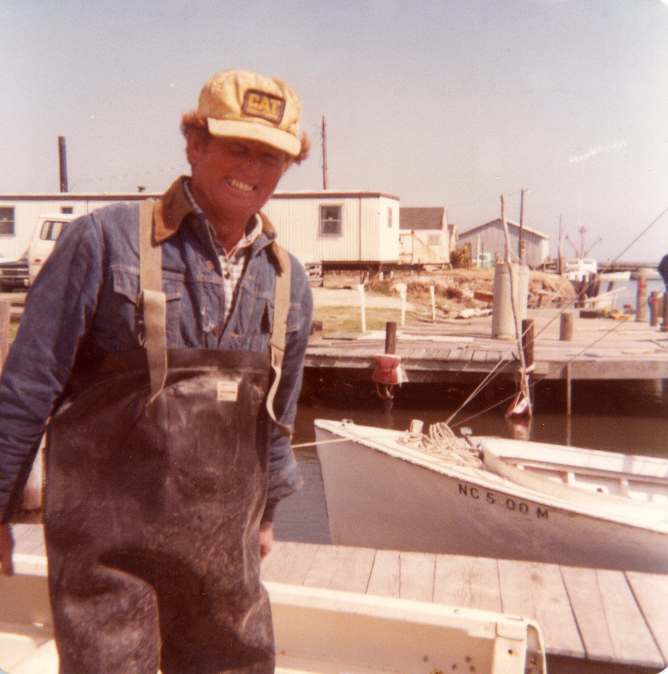 Red Brooks unloading clams at Miss Harkers Harbor, Clayton Fulcher’s Fishhouse in background, 1978.
