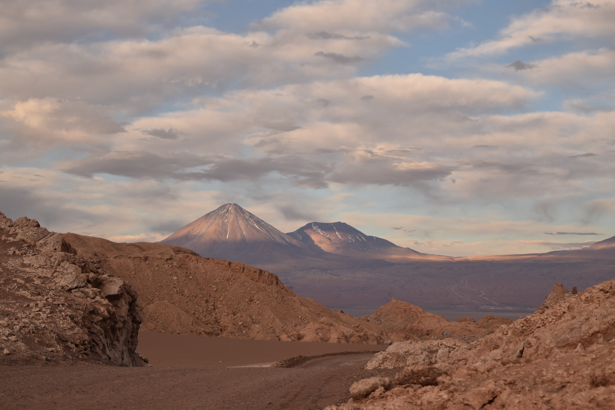 A barren landscape under a cloudy sky in the desert outside of San Pedro de Atacama, with the mighty Licancabur volcano rising in the distance.