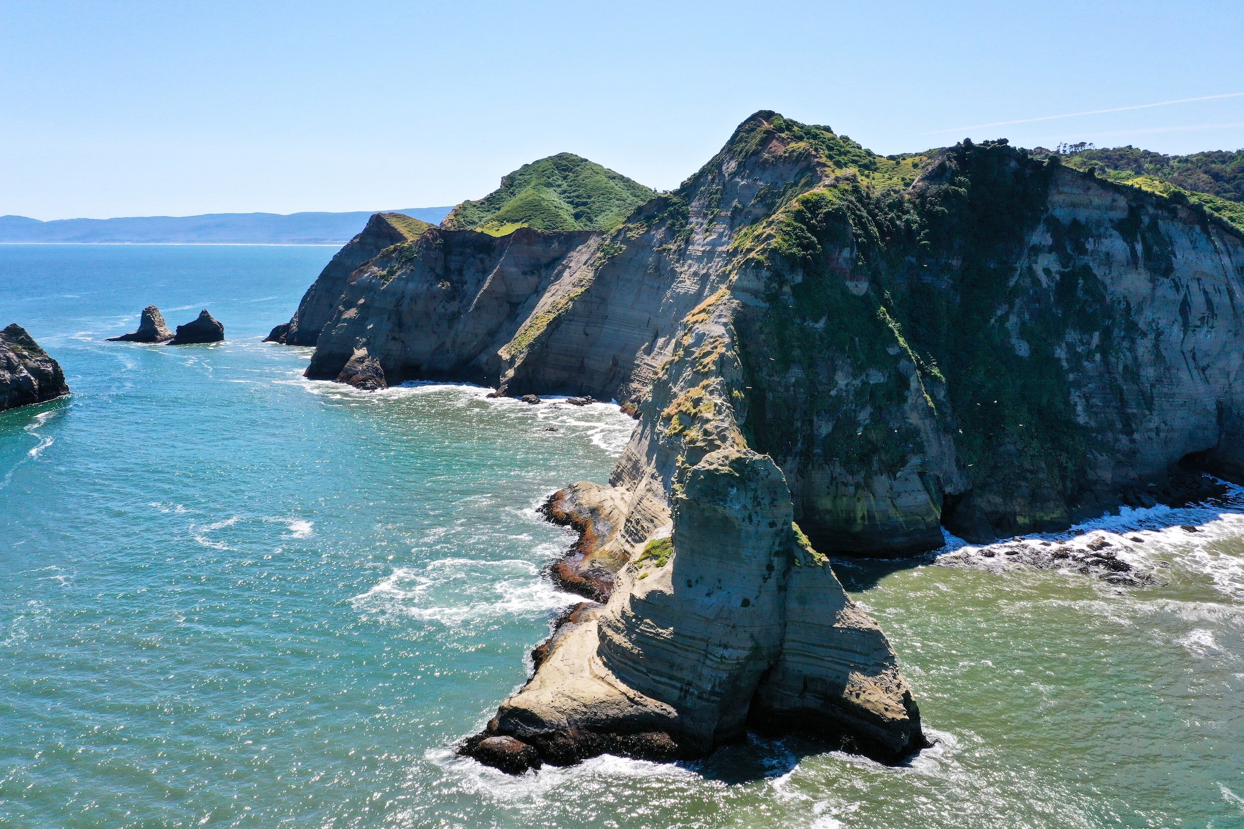 A green-topped outcrop of cliffs jutting into the sea on the coast of Chiloe island.