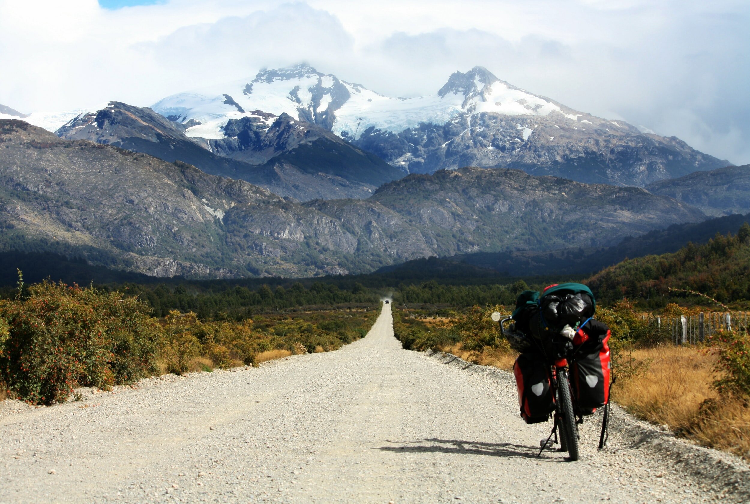 A bicycle laden with bags on an unpaved stretch of the Carretera Austral backed by towering snowcapped mountains in Chile.