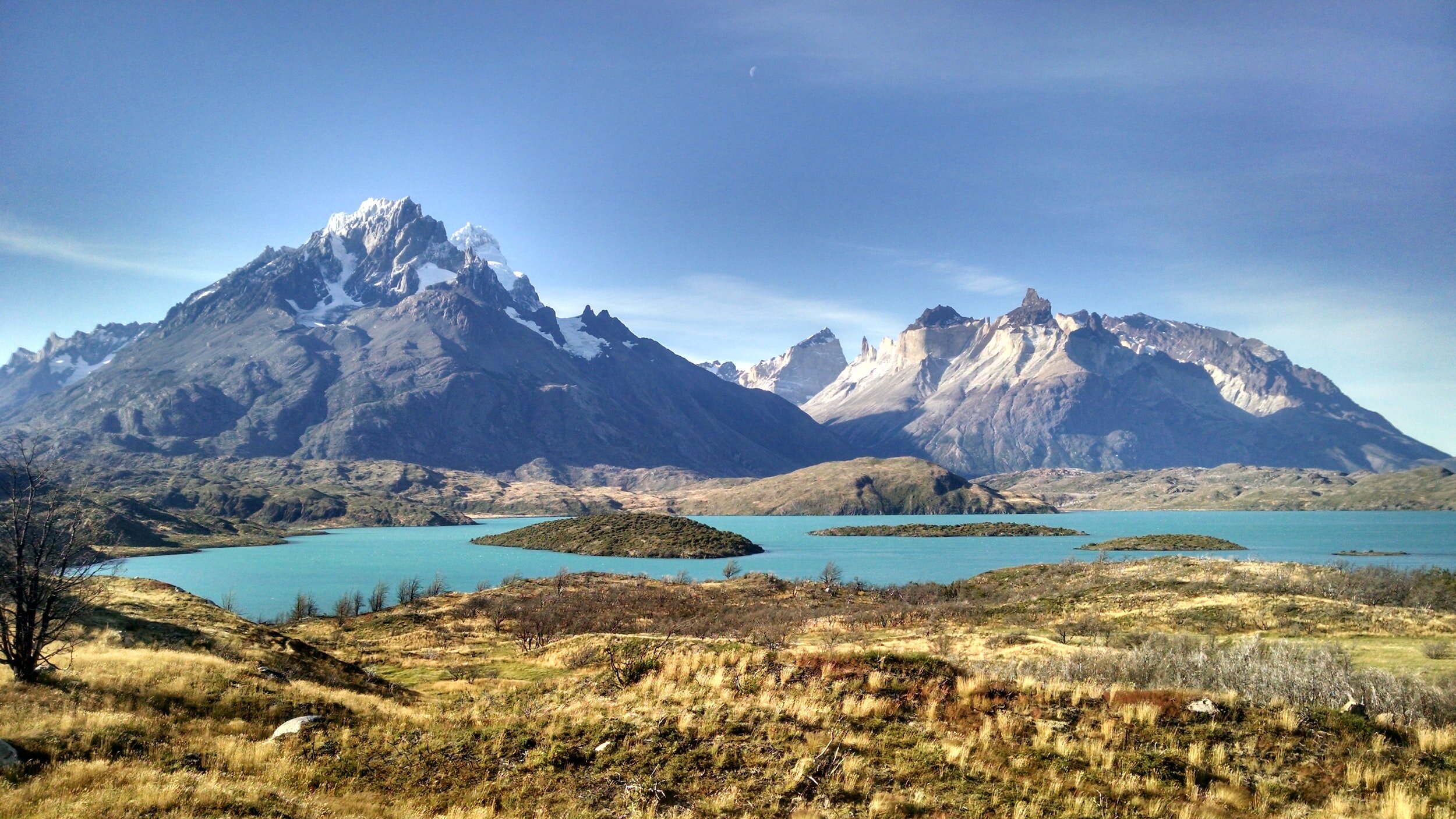 Torres del Paine's majestic, craggy peaks rise over  a grey-blue lake backed by almost yellow, windswept scrub.