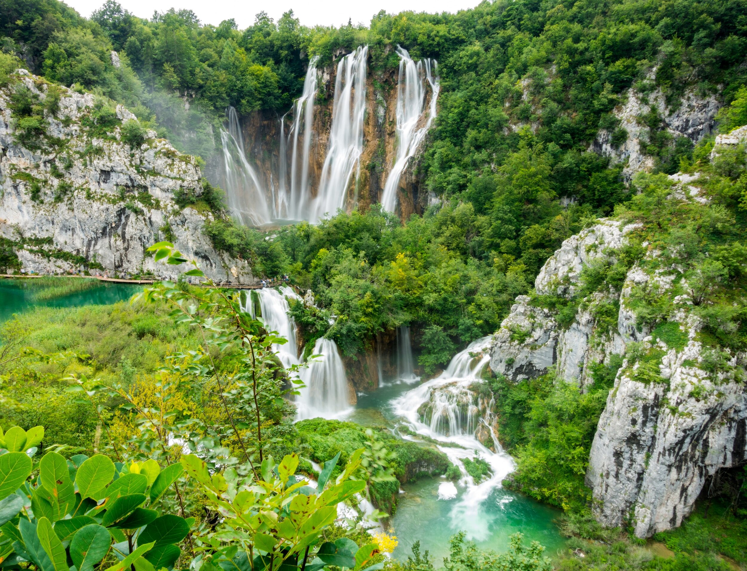 A waterfall surrounded by grey rocks and lush greenery in Plitvice Lakes National Park
