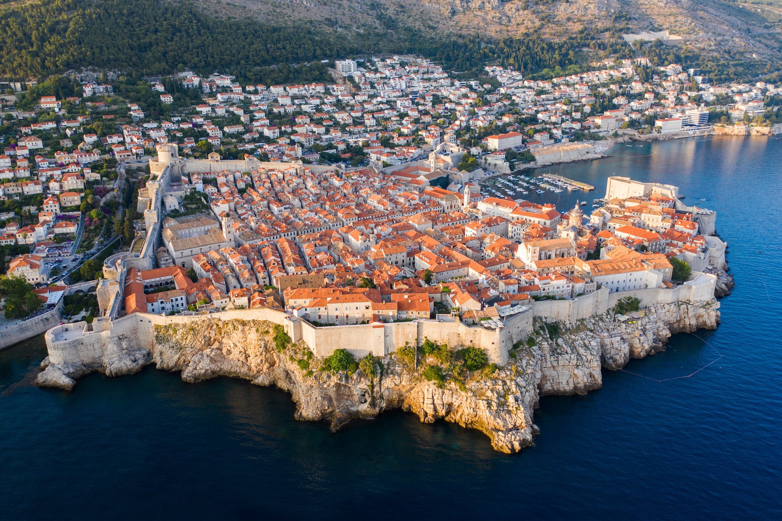 Dubrovnik's red tile roofs and historic core, surrounded by walls and jutting out into the water, seen from above.