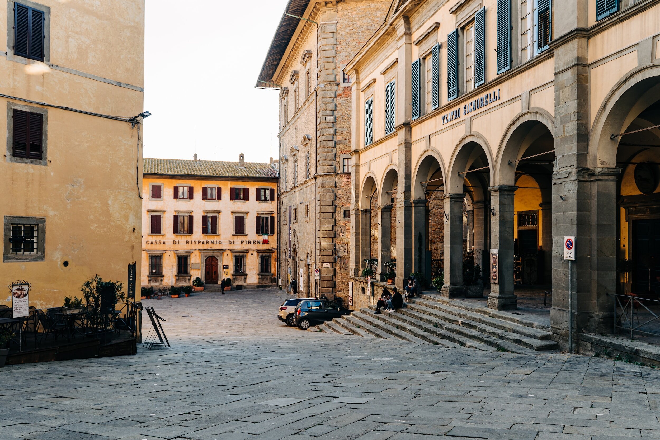 A pedestrian-only street and square in the city of Cortona, with a covered arcade on the right among other surrounding buildings