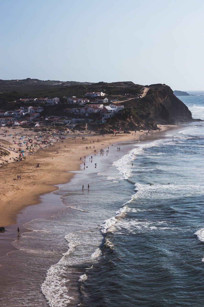 Waves crash on a crowded sandy beach at Monte Clerigo beach near to the town of Aljezur in the Algarve.