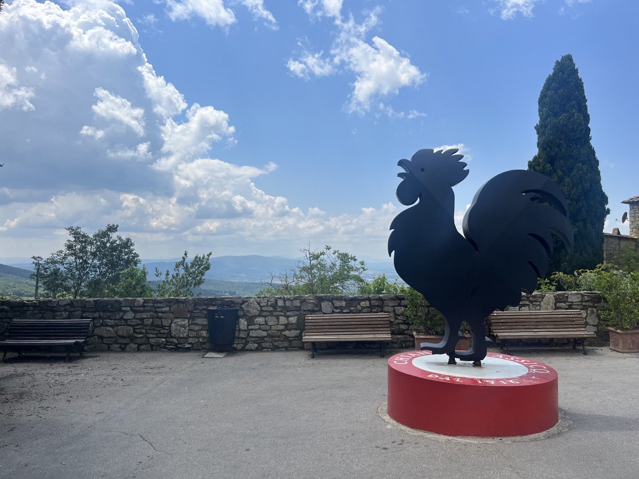 A giant black rooster statue on a red base with the words "Chianti Classico" stamped on it in front of a lookout point in the town of Castellina in Chianti.