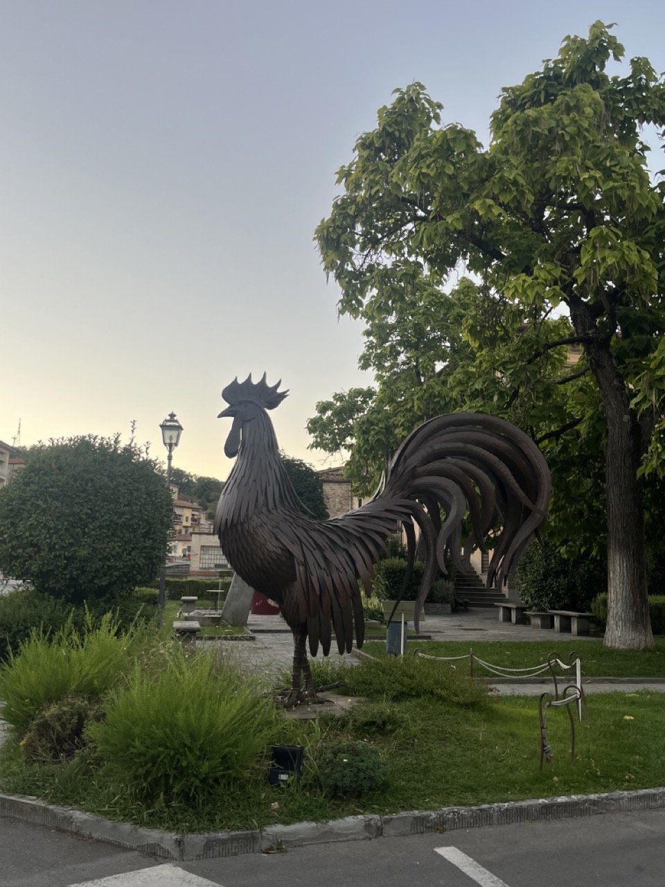 A close up view of a giant bronze rooster statue in a park in Gaiole in Chianti.