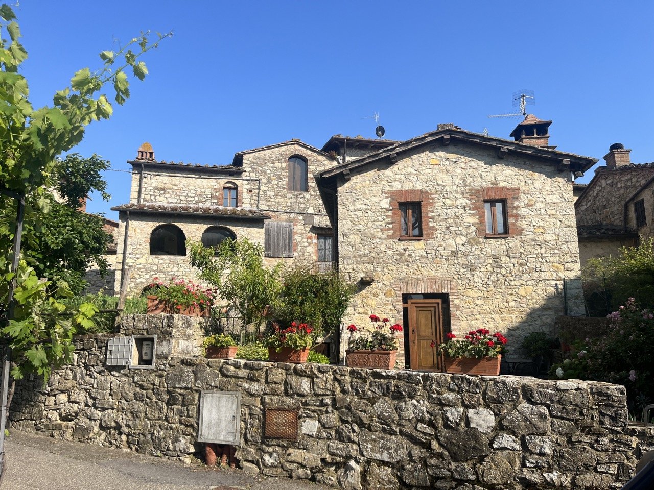 A stone wall in front of a lovely grouping of stone houses with wooden shutters and stone roofs in the small hamlet of San Sano in Tuscany's Chianti region.