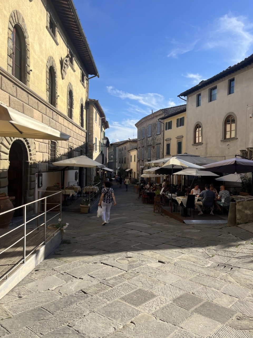 A pedestrian street lined with shops and restaurants featuring outdoor tables and umbrellas in Radda in Chianti.