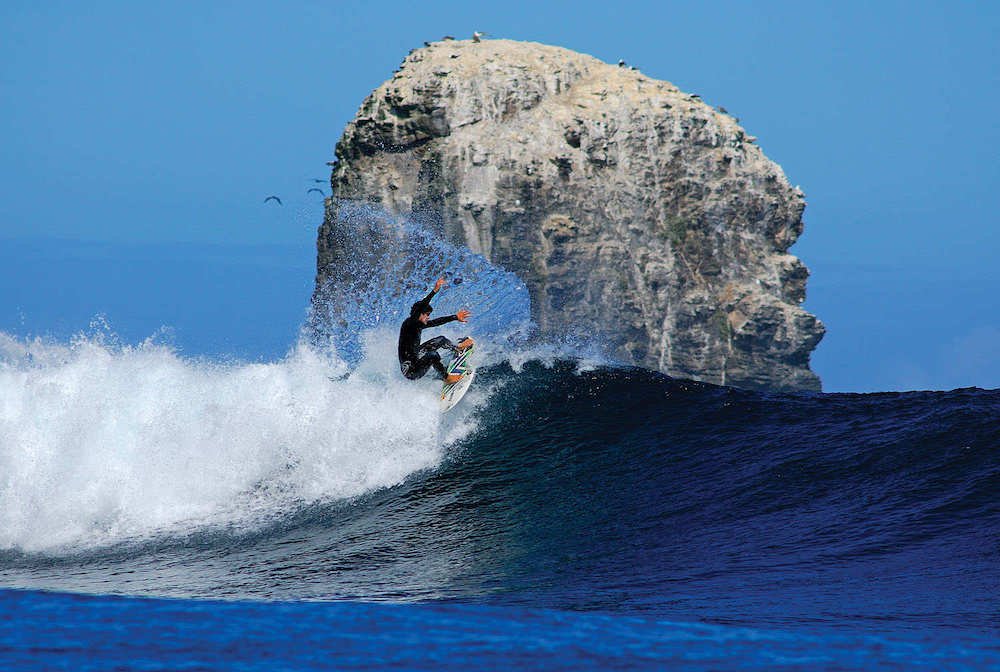A surfer rides a wave, in the shadow of a huge stone mastiff, at Punta de Lobos beach.