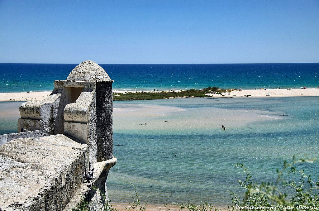 A stone walkway and watchpoint sit overlooking the clear blue waters and sandy beach at Cacela Velha fortress in the Algarve.