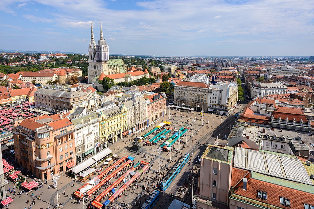 A market filled with people in a Central Zagreb square surrounded by elegant buildings seen from high above.