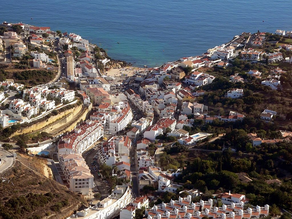 An aerial view of the town of Carvoeiro, Portugal, looking down on its white buildings and red roofs, winding out toward the ocean in the background