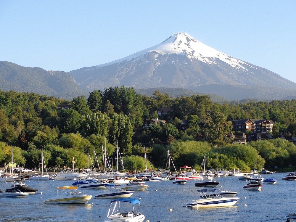 Snowcapped Villarica Volcano rises above Lake Villarica, full of small pleasure boats bobbing on its waters.
