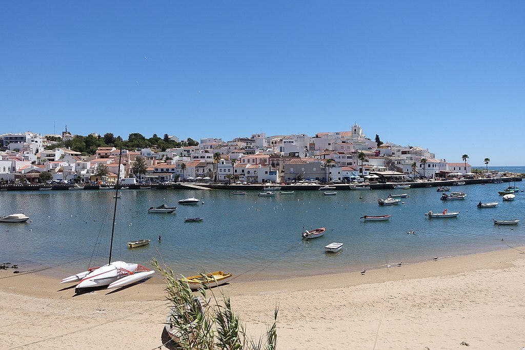 The town of Ferragudo, seen from the beach across from the town's harbor, which is filled with moored boats.