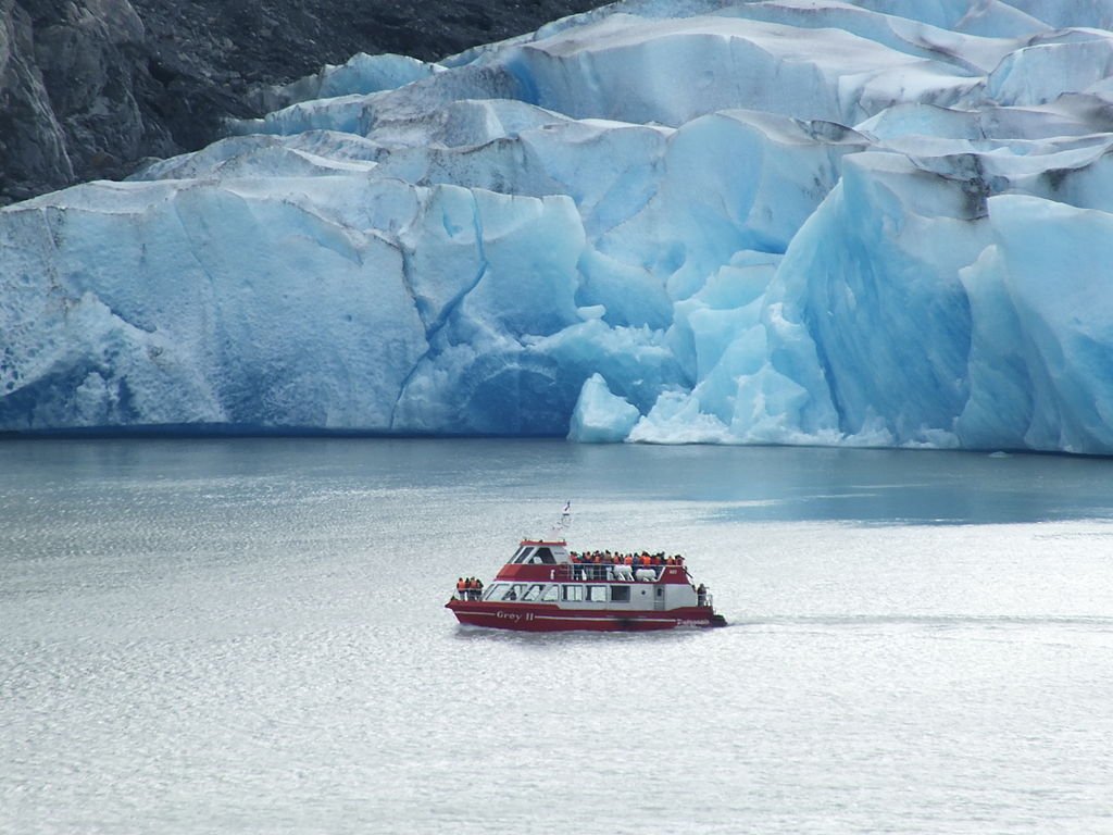A boat full of visitors on the viewing deck passes in front of a massive glacier in Torres del Paine park.