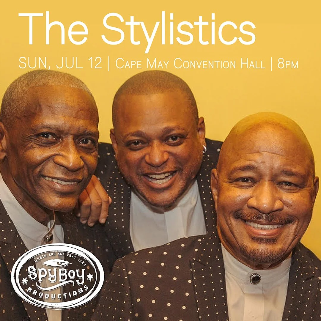 Poster for a music event called The Stylistics, happening on July 12 at Cape May Convention Hall at 8 PM. Features a photo of the three members of The Stylistics, smiling, dressed in black suits with white polka dots. The logo at the bottom left reads SpyBoy Productions.