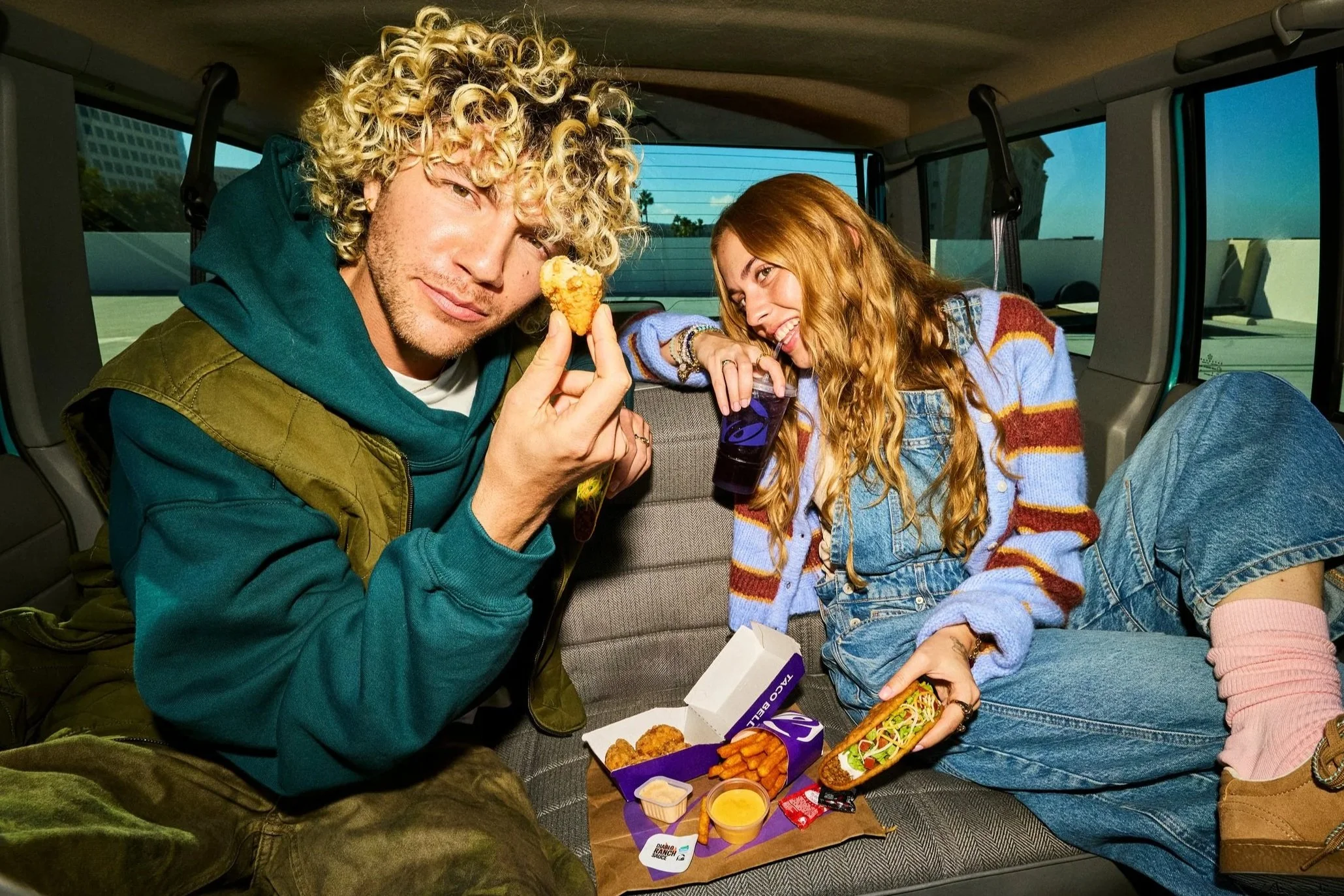 Two people in the back seat of a car eating Taco Bell