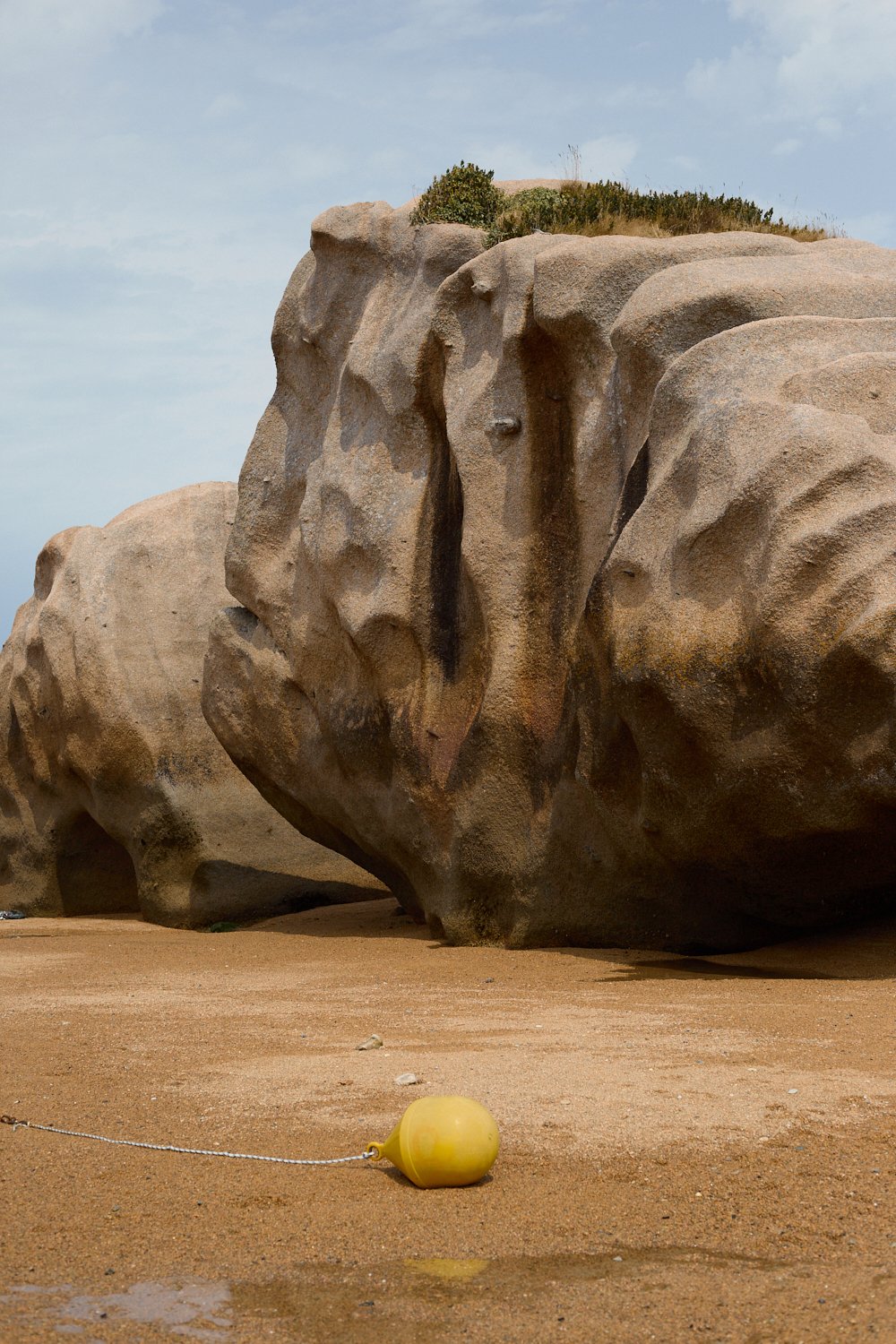 A large rock formation resembling a lion's face on a sandy beach with a yellow buoy in the foreground.