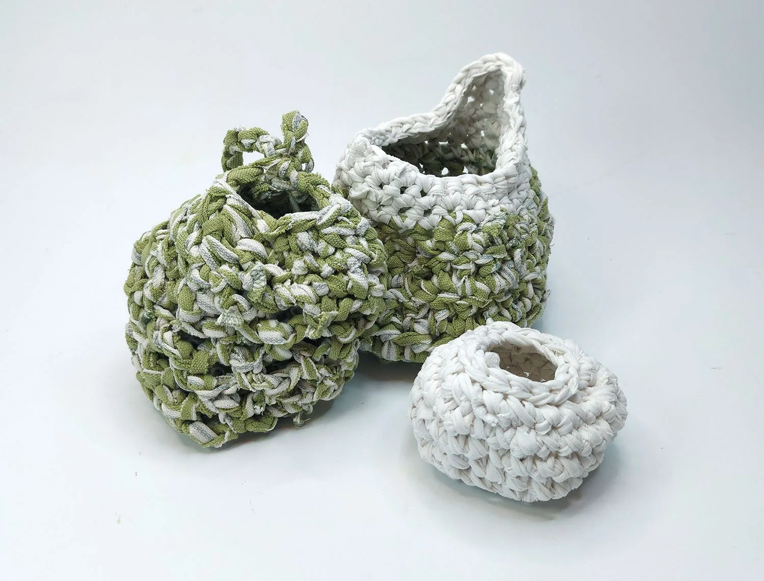 Three upcycled woven fabric baskets in white and green on a white background.