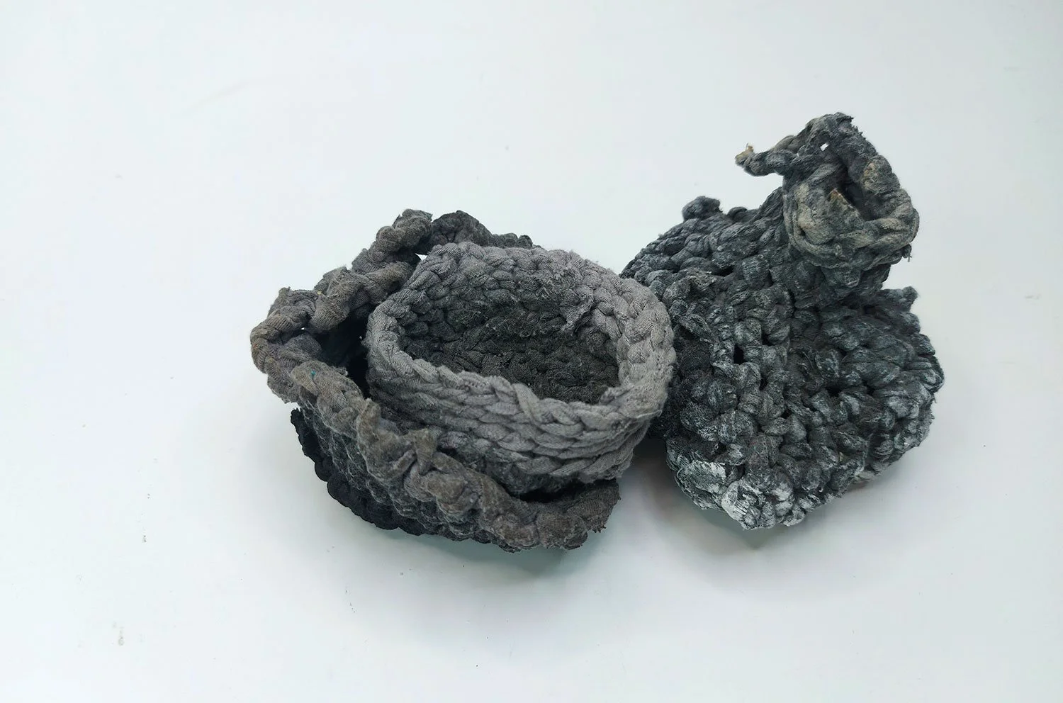 Three grey and black textured, vessels made from crocheted upcycled.