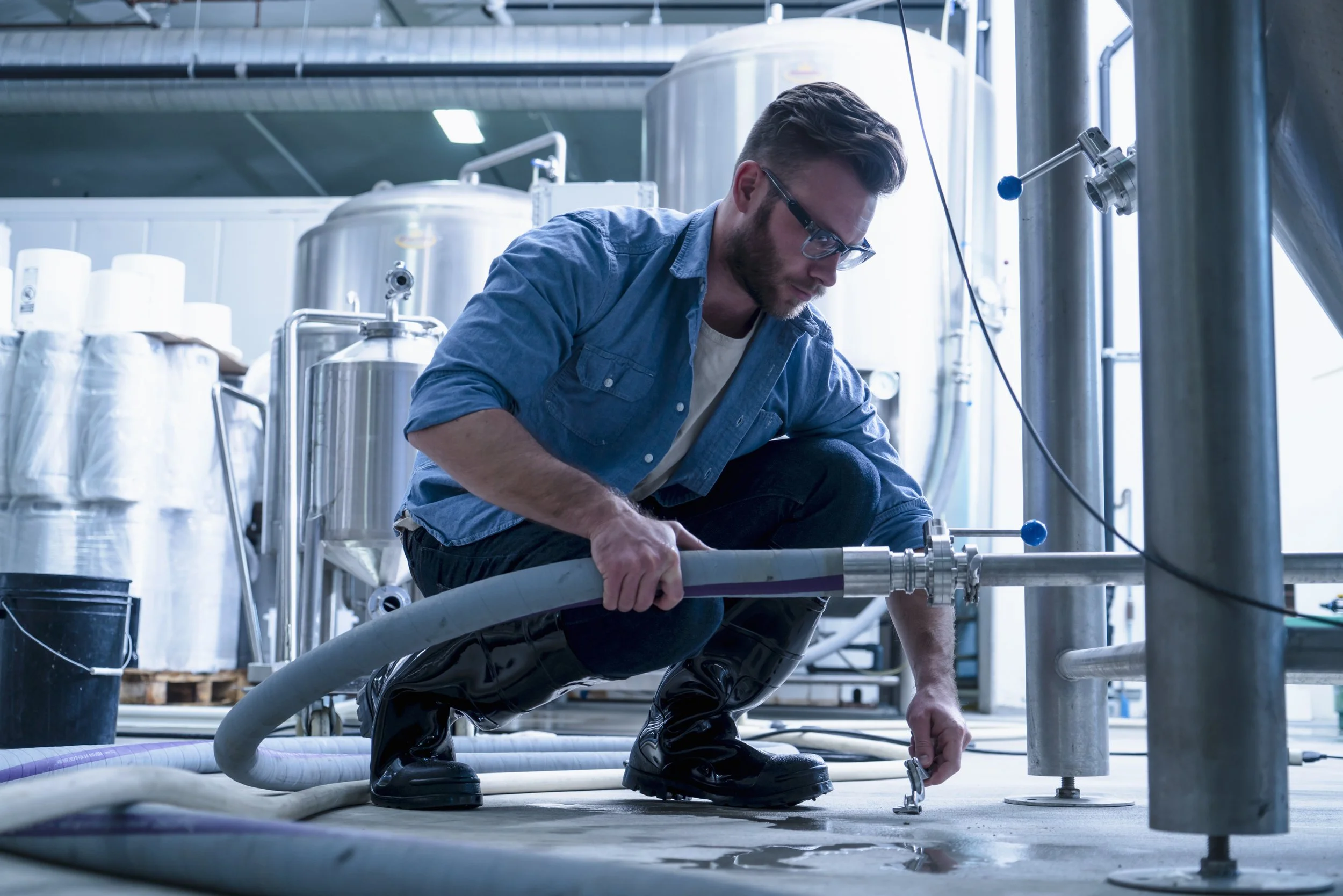 young-man-in-brewery-crouching-down-connecting-pip-2022-03-04-01-45-00-utc.jpg