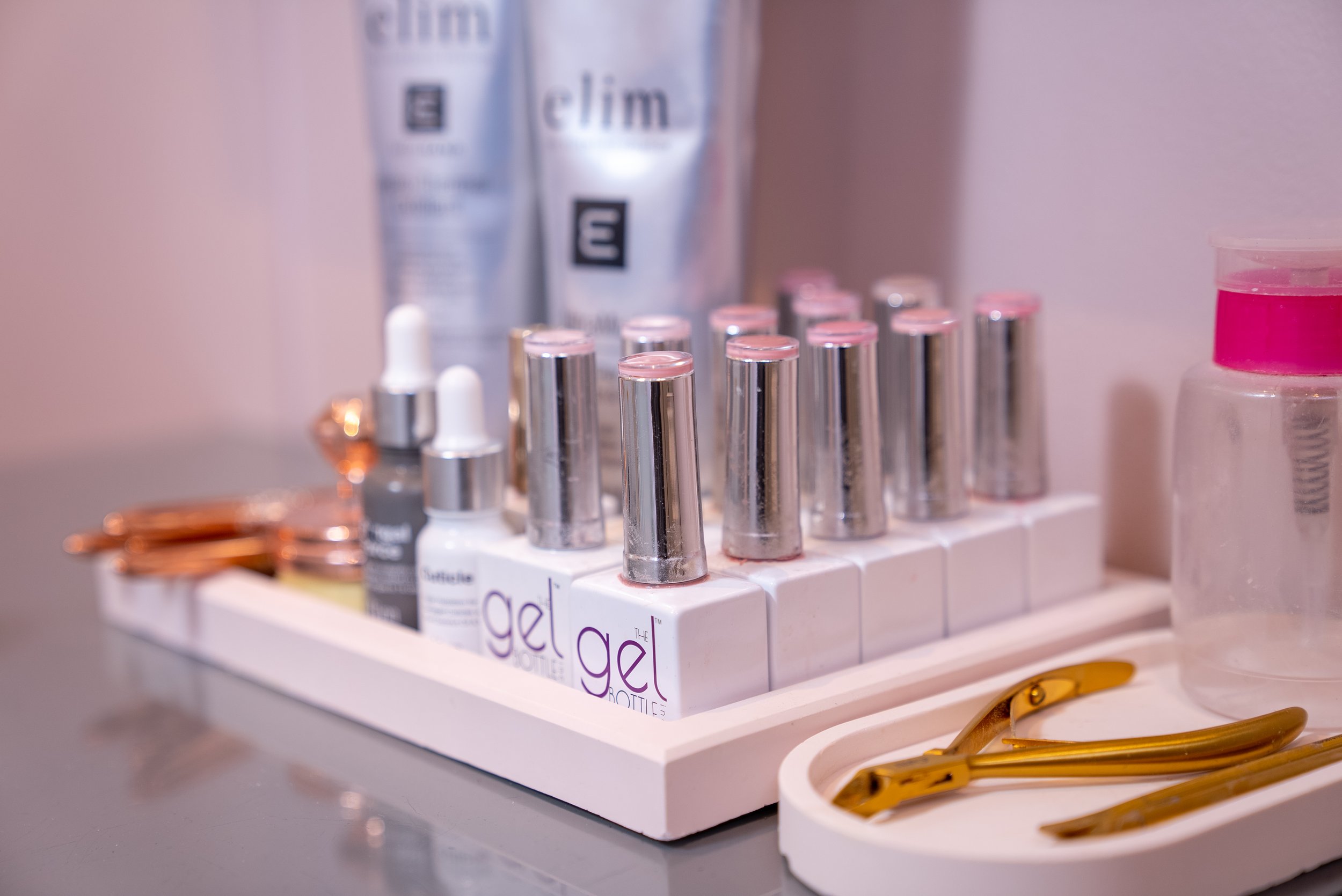Nail grooming tools, gel nail polish bottles, skincare products, and a liquid dispenser on a tray.