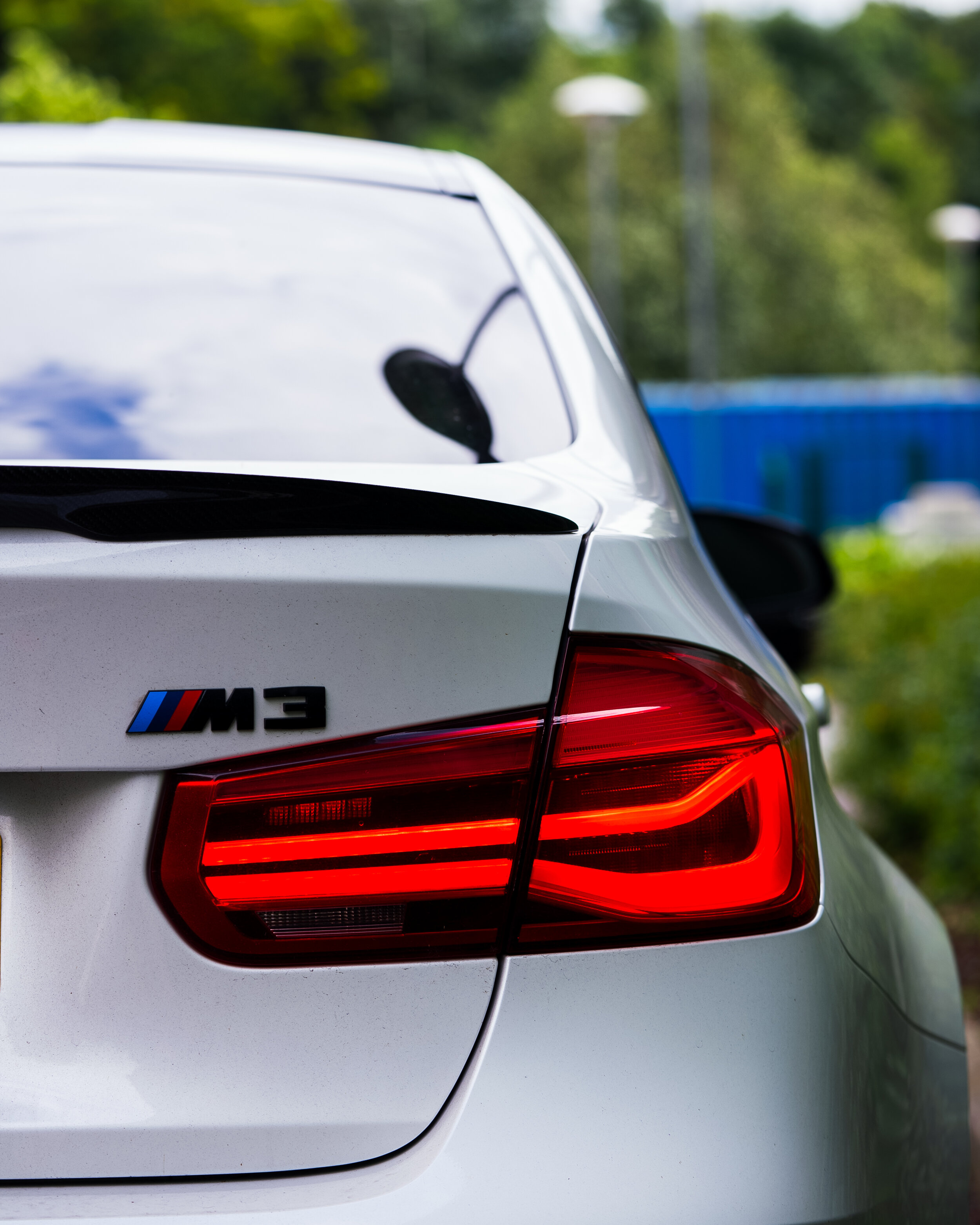 Rear view of a white BMW M3 with red taillights and M3 badge.