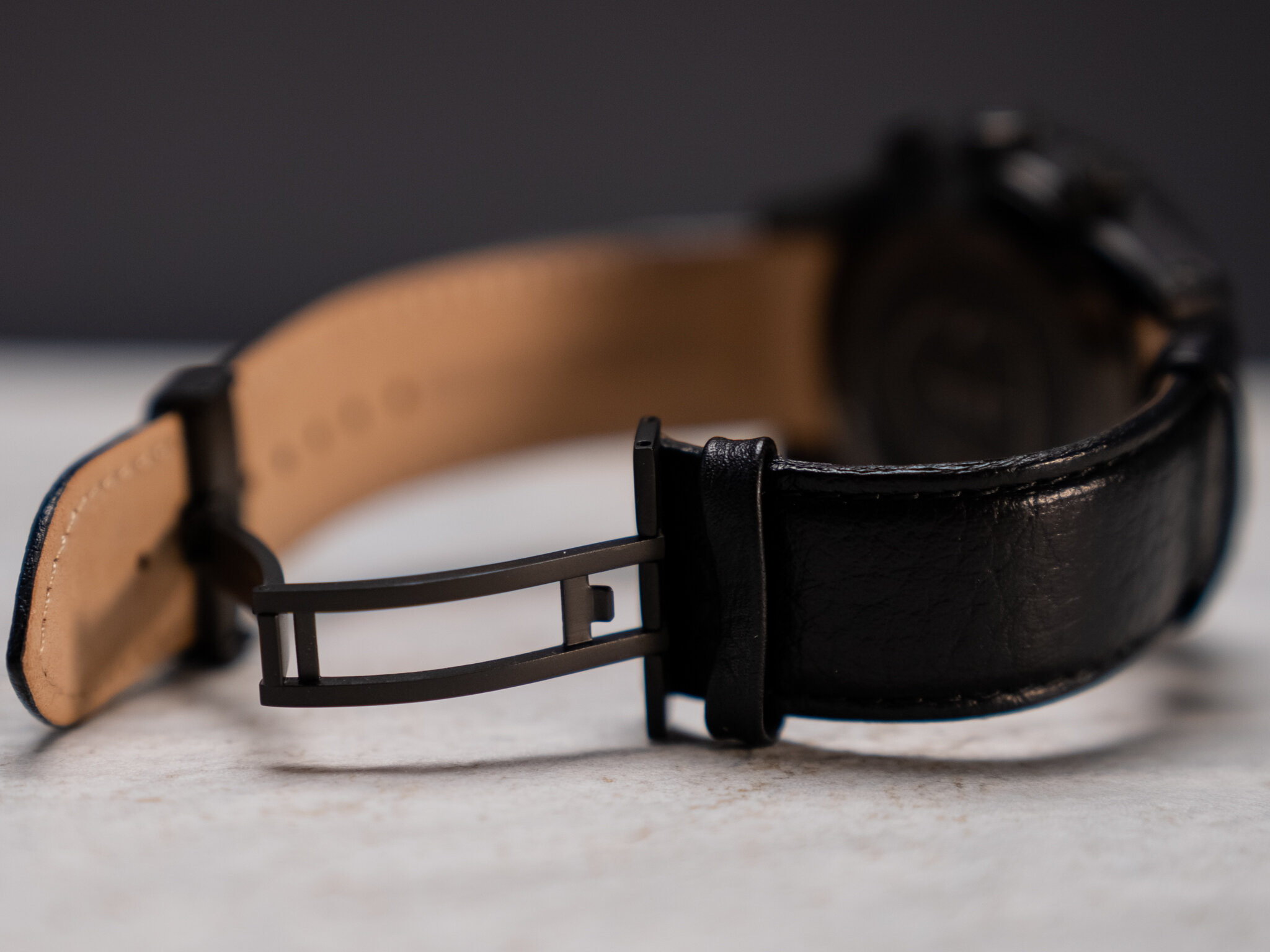 Close-up of a black leather watch strap with a metal clasp unbuckled.