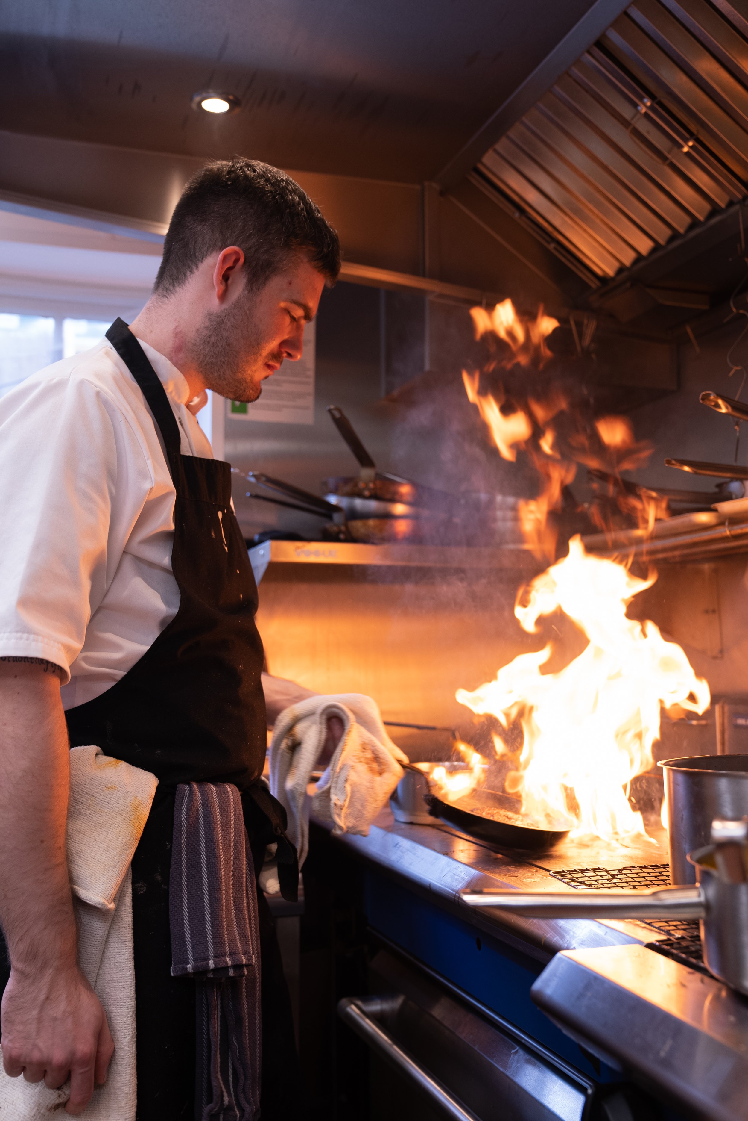 Chef cooking with flames in a professional kitchen.