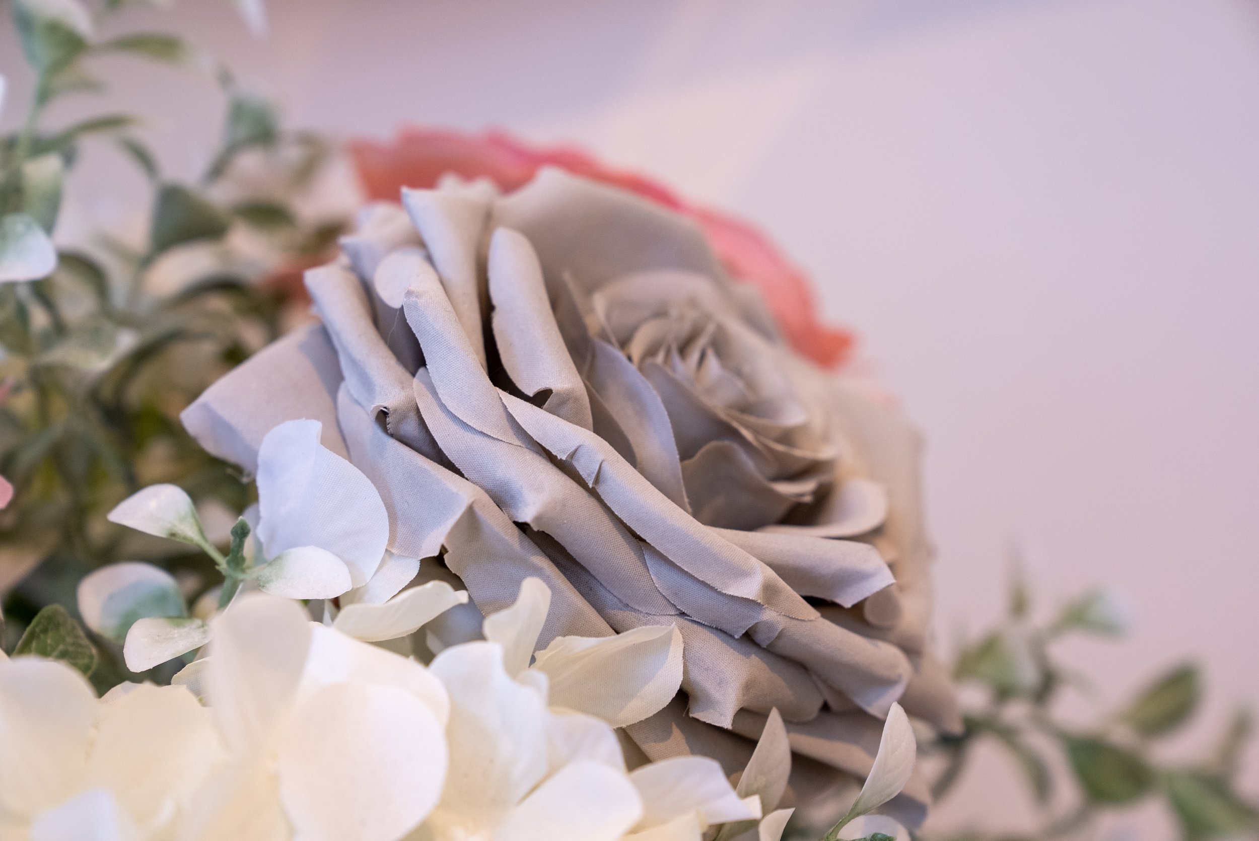 Close-up of a gray fabric flower with green leaves and white petals.