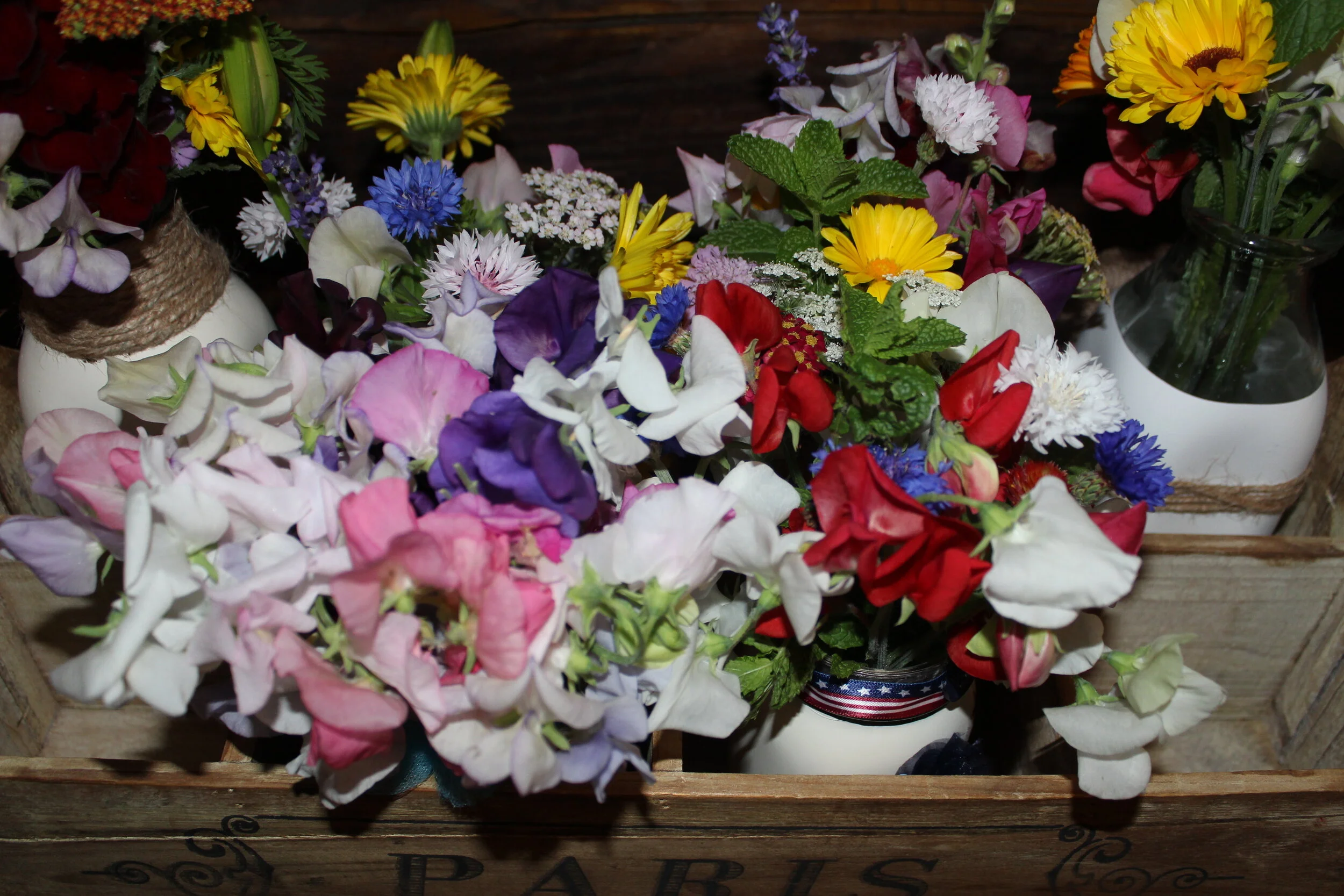 Assorted colorful flowers in a rustic wooden crate labeled 'Paris.'