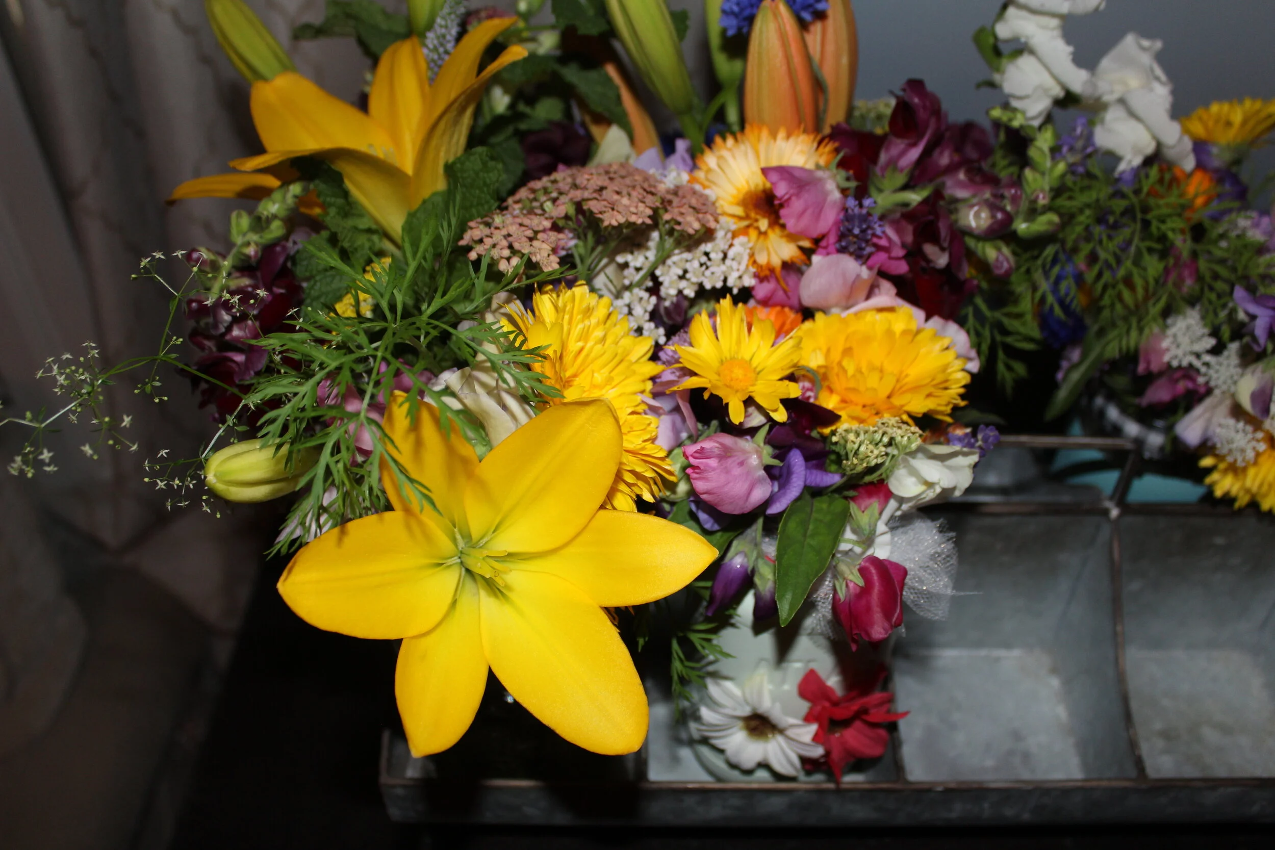 Colorful floral bouquet with yellow lilies, pink and purple flowers, green leaves, and various blooms in a vase.